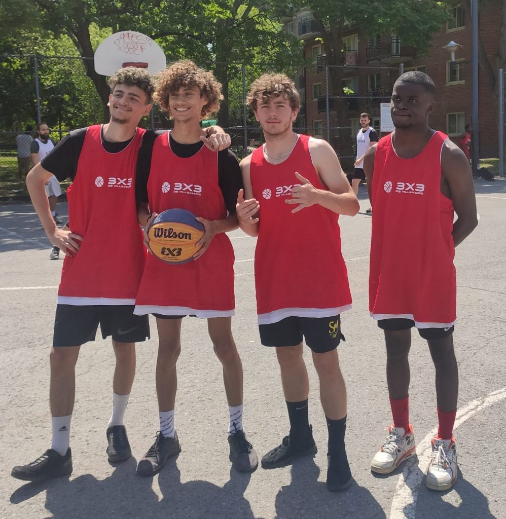 Photo de quatre garçons sur le city-stade dont un tenant un ballon de basketball 