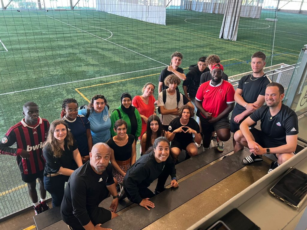 Douze jeunes, quatre encadrantes et trois professionnels se prenant en selfie devant un terrain de football indoor