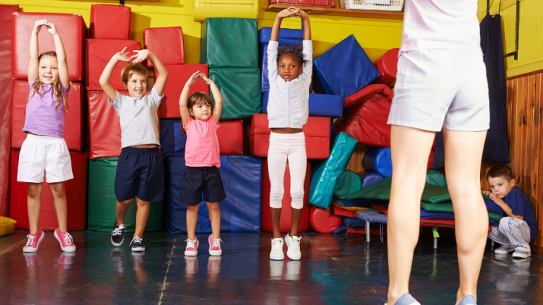 4 enfants s'exerçant aux étirements avec une éducatrice vu de dos