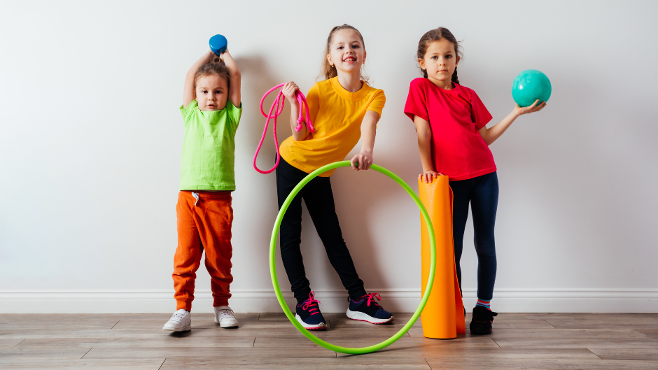 Trois enfants, deux filles et un garçon qui sont habillés en tenue de sport et pose avec un cerceau, une corde à sauter ou encore une balle
