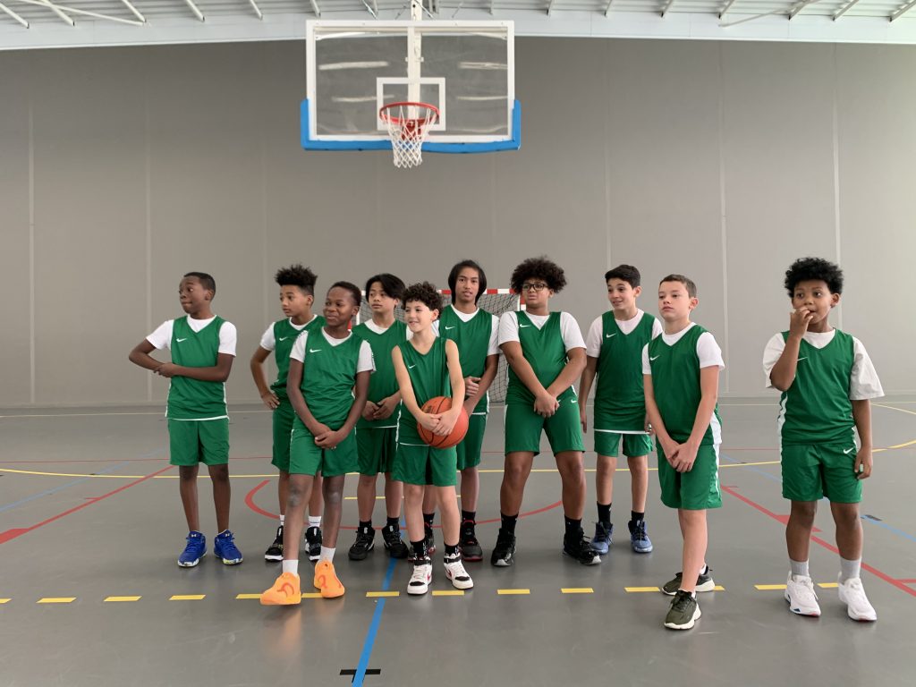 Photo d'enfant posant avec leur nouvelle tenue de Basket dans un gymnase du CSME Omnisports