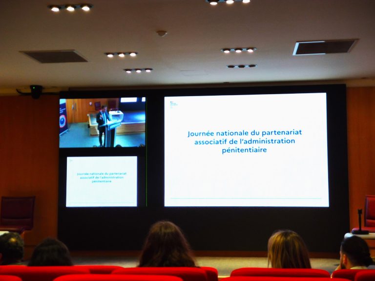 Participants assis en salle de conférence regardant une présentation diffusée sur grand écran