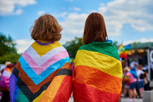 Deux femmes de dos portant sur leurs épaules le drapeau multicolore représentant les personnes LGBT+