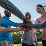 6 personnes issues de l'immigration en tenue de sport qui mettent leurs mains les unes sur les autres en souriant