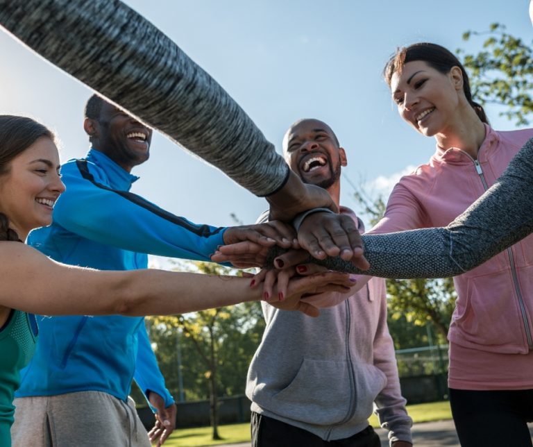 6 personnes issues de l'immigration en tenue de sport qui mettent leurs mains les unes sur les autres en souriant
