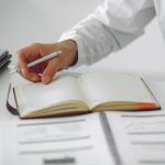 Close-up of a businessman writing notes in a diary at a modern office desk.
